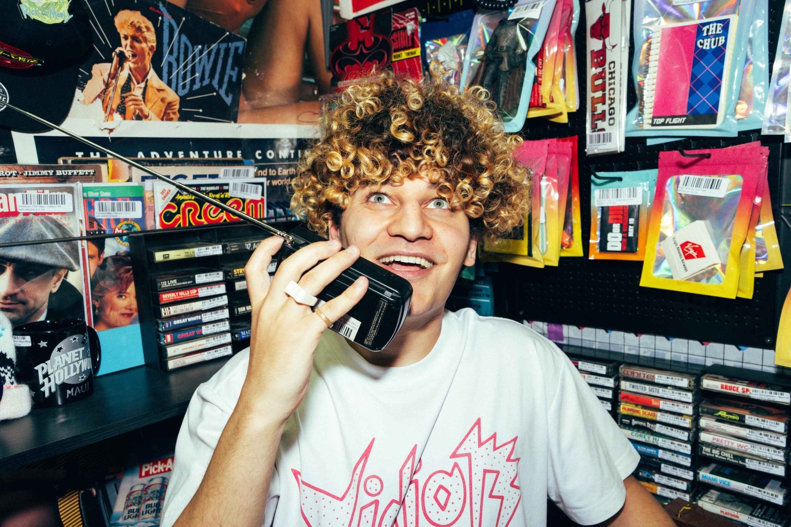 Dolo Tonight holding a phone in a colorful video store